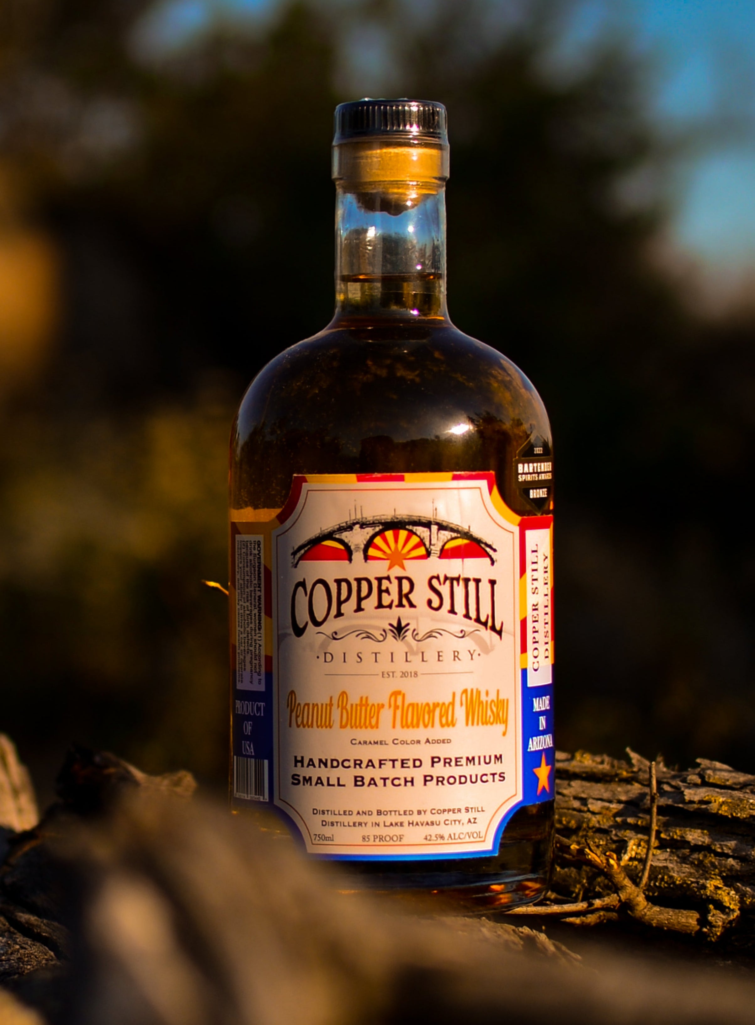 Bottle of Copper Still whiskey on a log with a blurred natural background